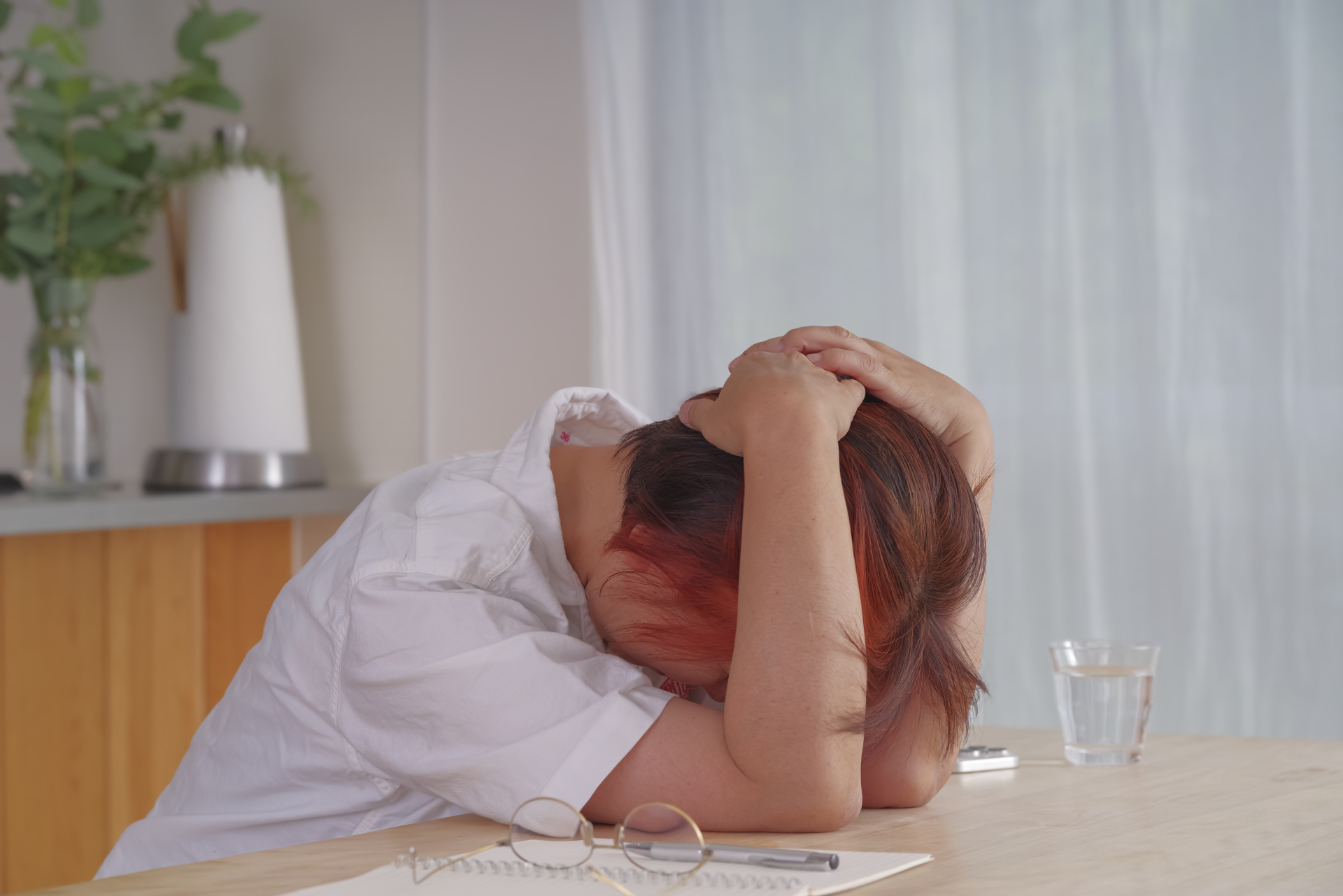 「疲れ果ててテーブルに伏せる中高年女性」（参考イメージ）
