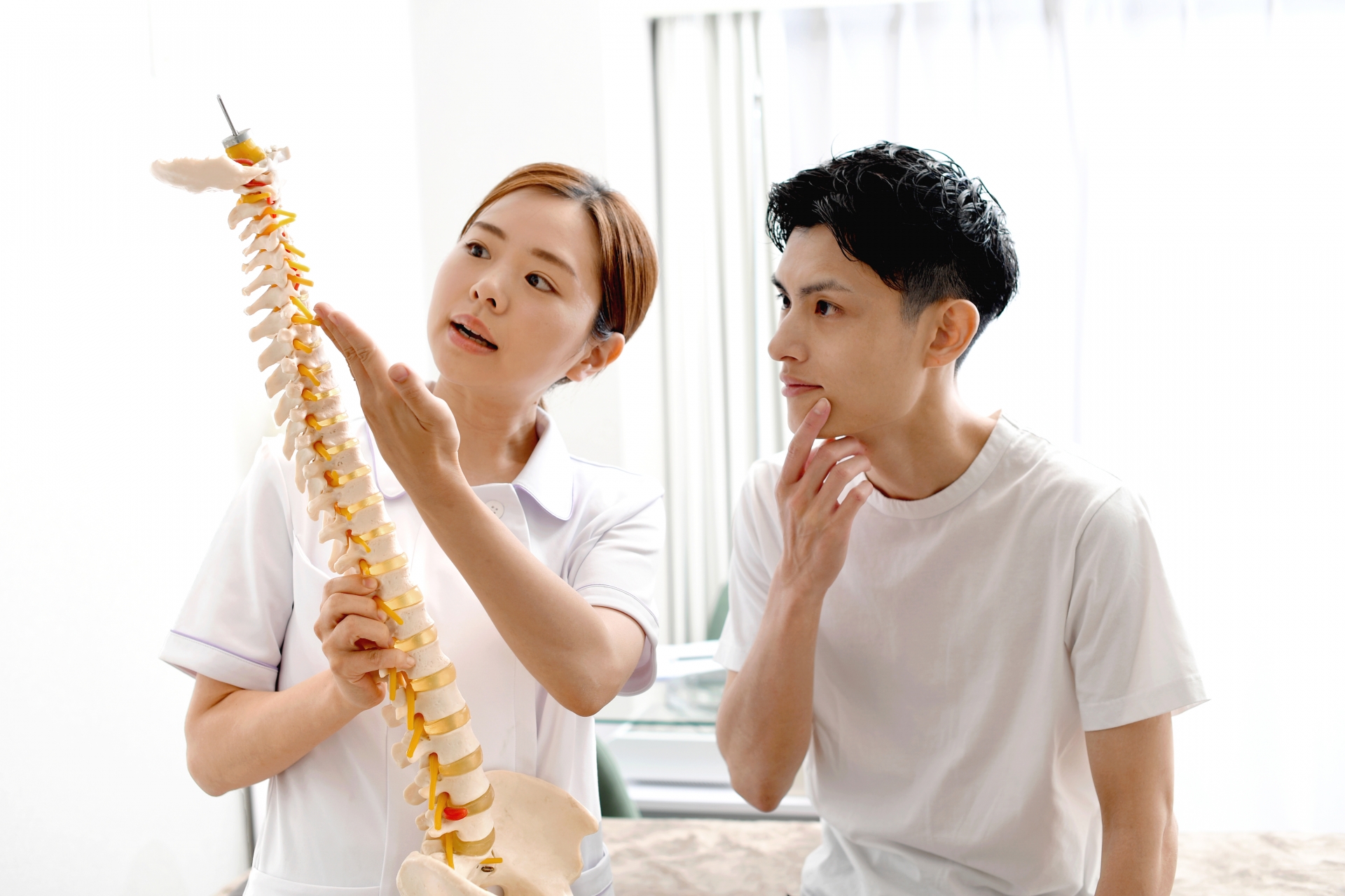 骨の模型を使い男性患者に説明する女性医師（参考イメージ）