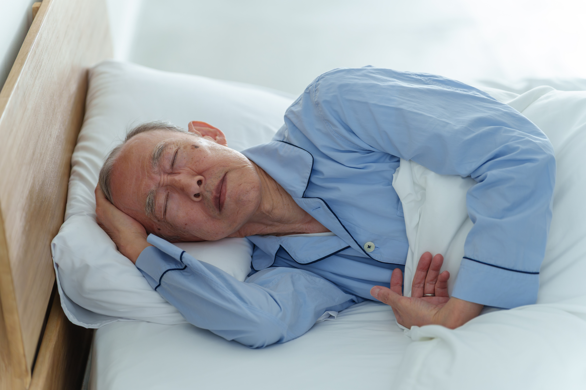 「ベッドで休む体調不良の高齢者の男性」睡眠・体調不良の表現。（参考イメージ）