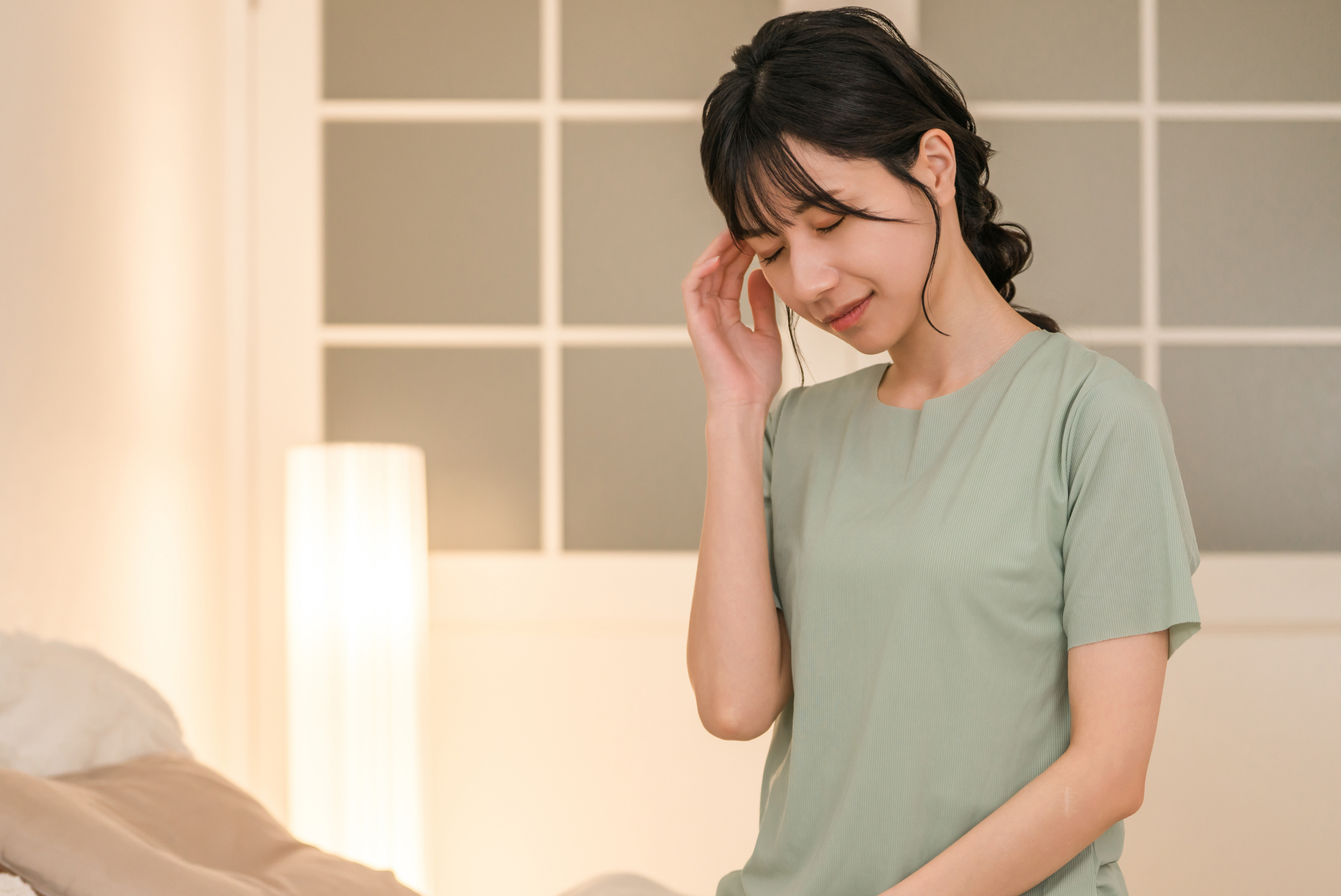 ベッドルームで寝起きに頭痛に悩む若い女性（参考イメージ）
